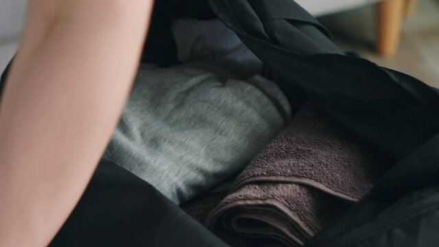 Active morning routine of young man, sport bag is being packed, getting ready to gym, putting all the necessary stuff inside: clothes, towel, cosmetic bag, bottle of water, accessories, Close up.