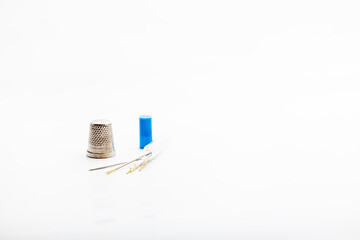 Minimalist detail of a silver metal thimble and needles of different sizes, used for sewing on a white background.