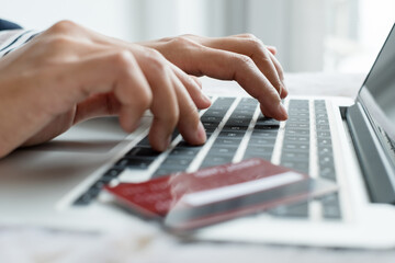 The businesswoman's hand is holding a credit card and using a laptop for online shopping and internet payment in the office