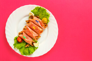 rolls with ham on a plate with green salad on a pink background. save a place