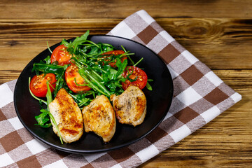 Fried chicken breast with salad of fresh arugula and cherry tomatoes on wooden table