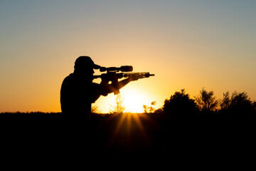 Silhouette of a man with a weapon in his hands on a sunset background