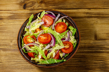 Healthy salad with savoy cabbage, cherry tomato, red onion and olive oil on wooden table. Top view