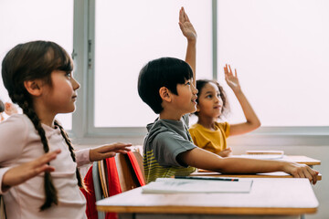 Elementary age Asian student boy raised hands up in Q and A class. Diverse group of pre-school...