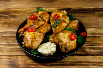 Roasted chicken drumsticks with spices in a black plate on a wooden table