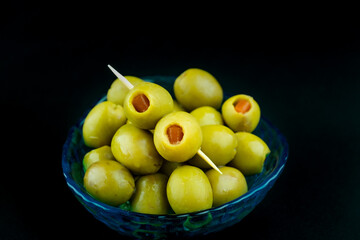Green olive with red chilli pepper preserved in the little blue bowl on black background