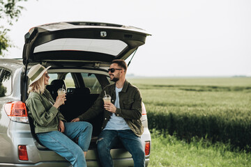 Man and Woman Sitting in the Trunk of Their Car and Drink Cold Coffee