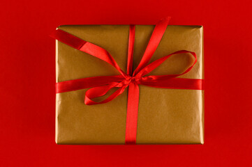 Wrapped gift box with ribbon bow as a present for Christmas, mother's day, anniversary, birthday, party, on red background.