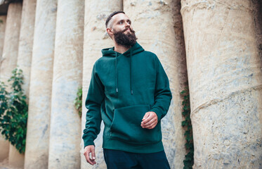 Obraz na płótnie Canvas City portrait of handsome hipster guy with beard wearing green (watercolor) blank hoodie or sweatshirt with space for your logo or design. Mockup for print