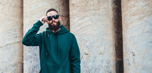 City portrait of handsome hipster guy with beard wearing green (watercolor) blank hoodie or sweatshirt with space for your logo or design. Mockup for print