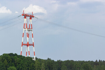 Big red-white High voltage tower over the forest. electricity pylons,cables and fencing on it. at...