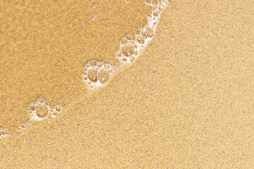 Fototapeta na wymiar Foamy and crystal clear sea wave on the warm beach sand. Place for design and text. Concept for New Year's vacation abroad for holidays 2020-2021.