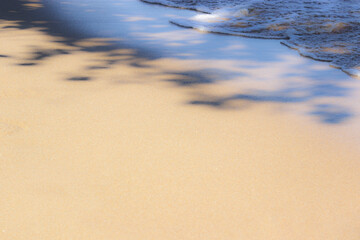 Foamy and crystal clear sea wave on the warm beach sand. Place for design and text. Concept for New Year's vacation abroad for holidays 2020-2021. This photo is a little out of focus