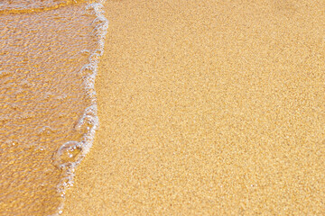 Foamy and crystal clear sea wave on the warm beach sand. Place for design and text. Concept for New Year's vacation abroad for holidays 2020-2021.