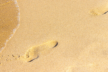 Clear sea wave on the warm beach sand and footprint of human on it. Place for design and text. Concept for New Year's vacation abroad for holidays 2020-2021. This photo is a little out of focus.
