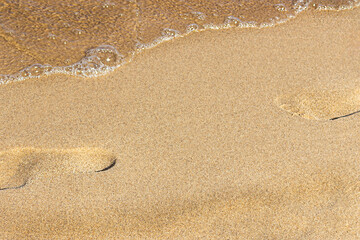 Clear sea wave on the warm beach sand and footprint of human on it. Place for design and text. Concept for New Year's vacation abroad for holidays 2020-2021. This photo is a little out of focus.