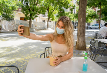 Woman wearing protective face mask on mobile video calling friends in coffee shop in the New Normal