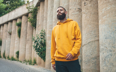 City portrait of handsome hipster guy with beard wearing yellow blank hoodie or sweatshirt with space for your logo or design. Mockup for print