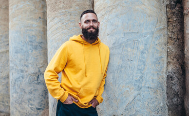 City portrait of handsome hipster guy with beard wearing yellow blank hoodie or sweatshirt with space for your logo or design. Mockup for print