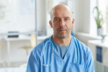 Medium close-up portrait shot of mature doctor wearing blue uniform looking at camera with serious facial expression
