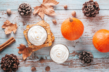 Autumn mood cozy flat lay with pumpkin latte, cedar pine cones, pumpkins and dried leaves on worn wood background, top view, fall, Thanksgiving background