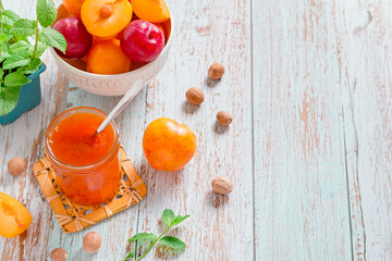 Yellow and red plums in a plate and jar of plum jam on worn wooden table flat lay, autumn fruit preserves concept, copy space