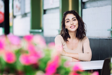 A young woman is sitting in a street city cafe. Beautiful smiling brunette.