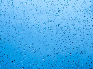 blue rain water drops on a window glass close up with sad clouds in background, drop macro texture...