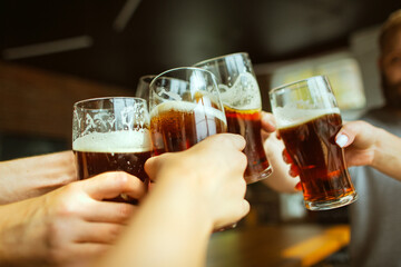 Close up clinking. Young group of friends drinking beer, having fun, laughting and celebrating together. Women and men with beer's glasses. Oktoberfest, friendship, togetherness, happiness concept.