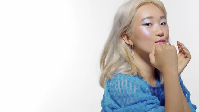 closeup portrait of blonde korean model with shiny makeup poses to the camera with hair blowing in bright blue blouse