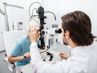 Practicing ophthalmologist examines a senior woman patient’s with special ophthalmic equipment in a modern clinic. Vision correction of elderly people