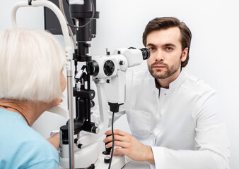 Optometrist doctor using a binocular slit-lamp examines the eye of an elderly woman patient. Aged people must be tested by an ophthalmologist
