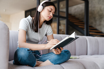Obraz premium Image of focused asian woman using headphones and writing down notes