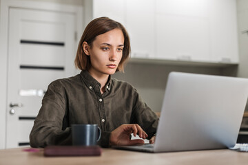Young woman in shirt works at home using laptop