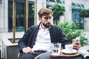 Serious pensive man using smartphone in cafe