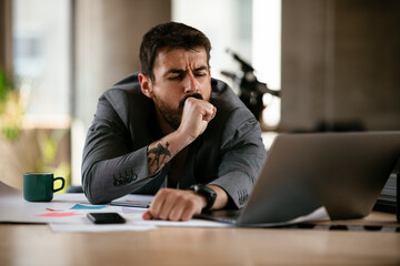 Fototapeta premium Tired businessman working with laptop at office. Businessman sitting at office desk working on laptop computer...