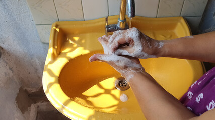 washing of both hands with soap under a yellow wash basin with running tap water to produce foam and lather