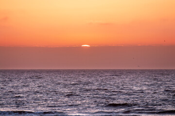 Fototapeta premium Sun disappearing behind clouds at sunset on the coast of Holland