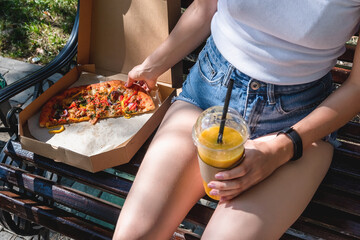 Beautiful, young woman eating pizza and fries in the street. The concept of fast food, food delivery and lunch in nature