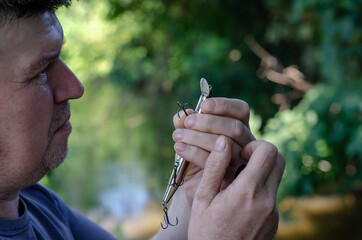 An adult man carefully examines a fishing hook on a wobbler.