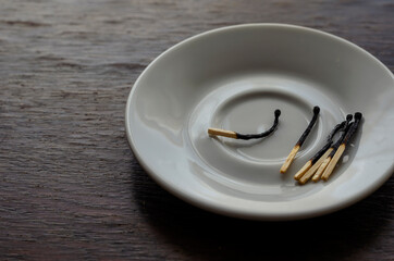 A white saucer with several burnt matches on a wooden table.