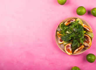Lime and blood orange slices, ice, mint leaves over pink background. Citrus ingredients for fresh summer iced cocktail. Copy space