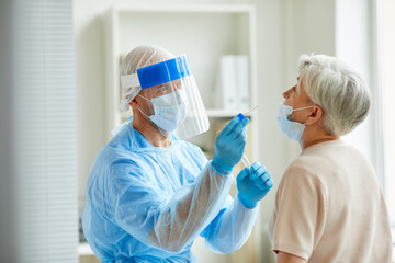 Modern laboratory worker wearing personal protective equipment testing senior woman for coronavirus...