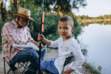 grandfather and grandson fishing outdoor on the lake, little boy looking at the camera