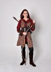 Full length portrait of girl with red hair wearing  brown medieval archer costume.. Standing pose...