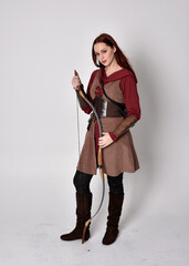 Full length portrait of girl with red hair wearing  brown medieval archer costume.. Standing pose...