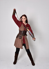 Full length portrait of girl with red hair wearing  brown medieval archer costume.. Standing pose...
