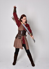 Full length portrait of girl with red hair wearing  brown medieval archer costume.. Standing pose...