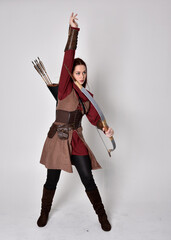 Full length portrait of girl with red hair wearing  brown medieval archer costume.. Standing pose...