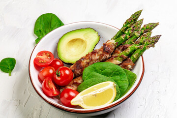 Bowl Buddha. Asparagus baked with bacon and tomatoes with herbs, avocado on a light background, top view